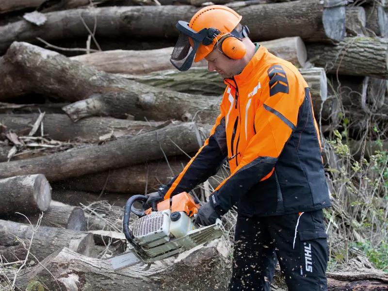 Ein Facharbeiter von Göschlholz bei der Aufarbeitung von Stammholz mit einer Motorsäge vor einem großen Holzpolter.